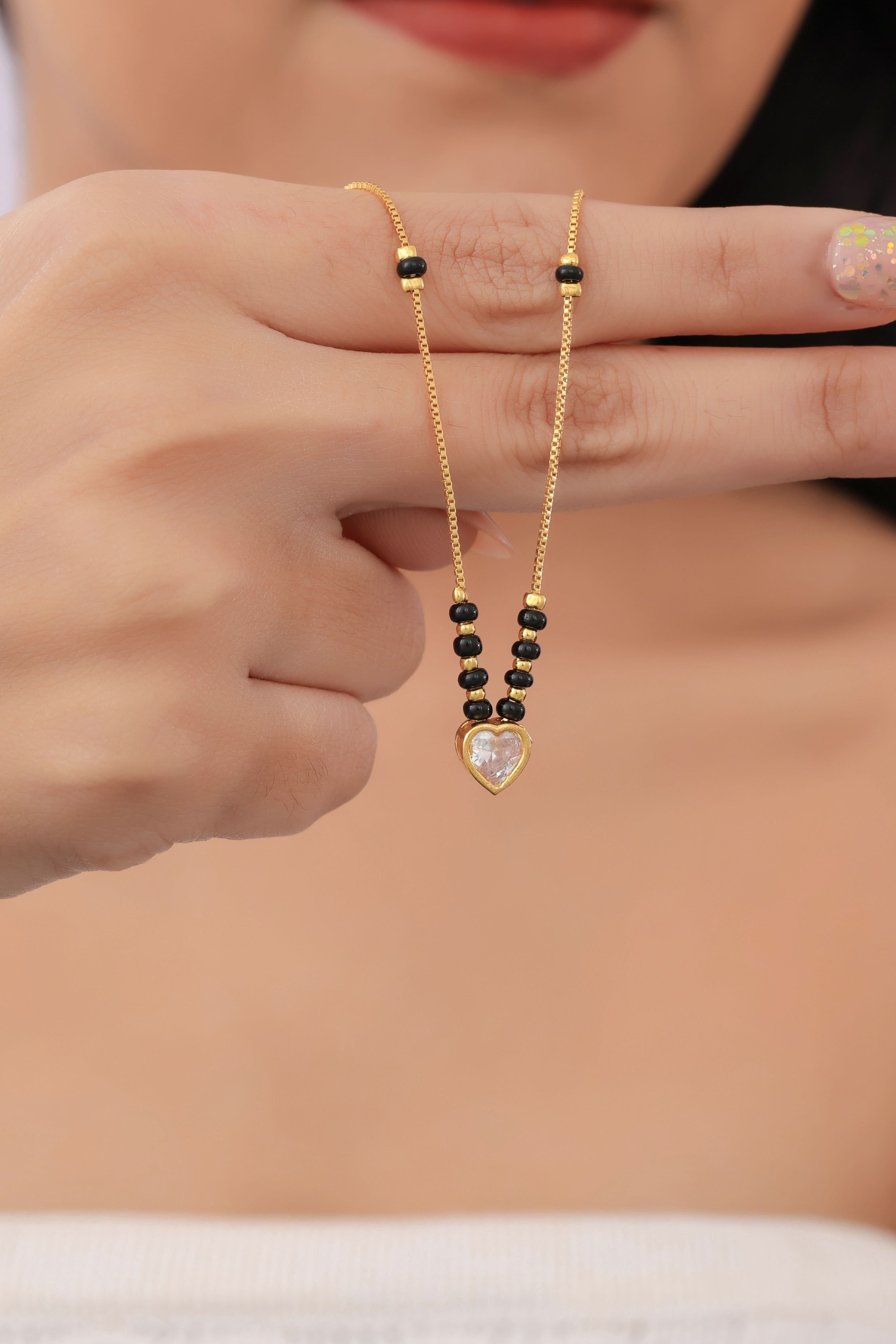 Gold necklace with black beads held by a person