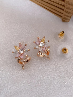 Pair of gold and pink star-shaped earrings on a white surface with a wooden stand in the background.