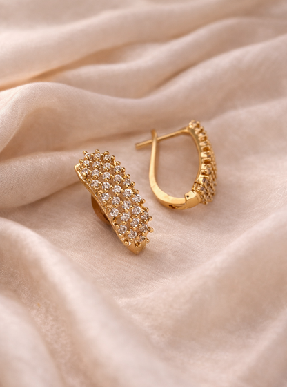 Gold hoop earrings with embedded stones on a soft beige fabric background