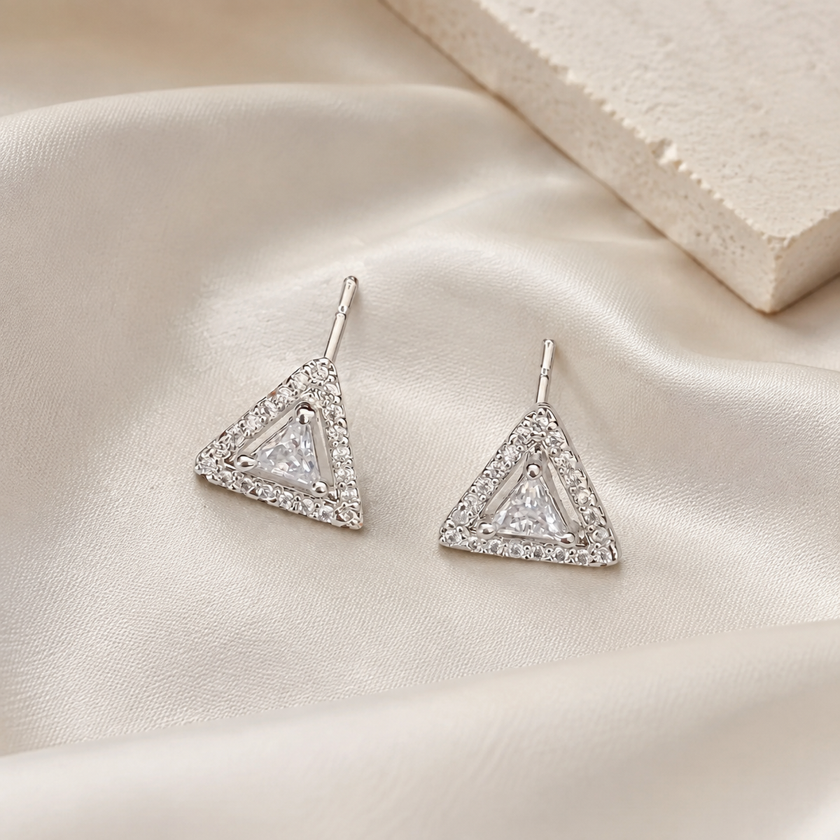Silver triangular stud earrings on ivory silk