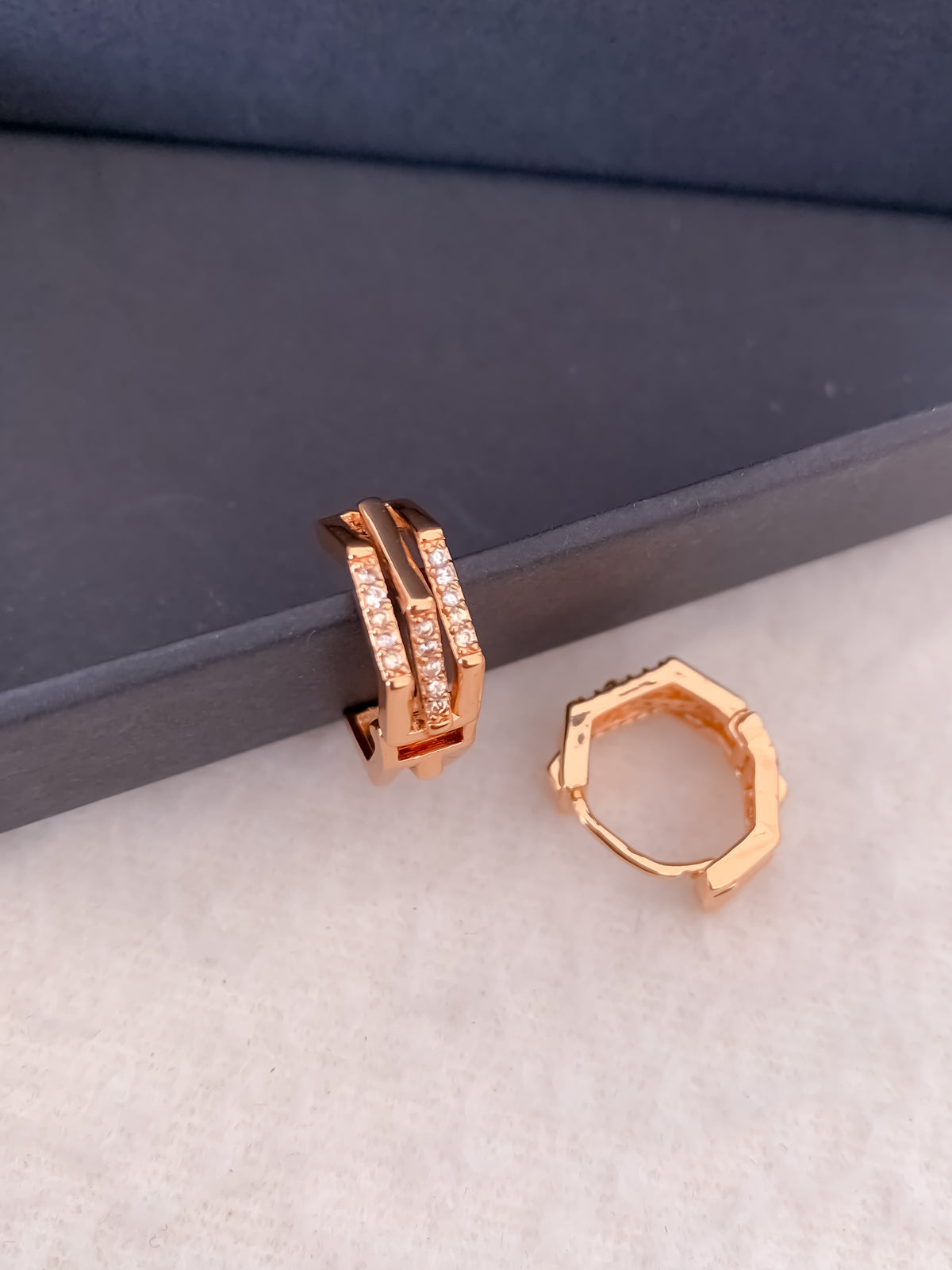 Rose gold hoop earrings on a textured surface with a blue background, Belleza Jewels