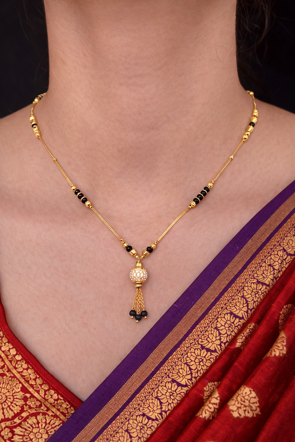 Gold necklace with black beads worn by a person in a red and gold saree.