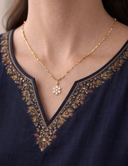 Gold necklace with a floral pendant on a person wearing a dark blue embroidered garment.