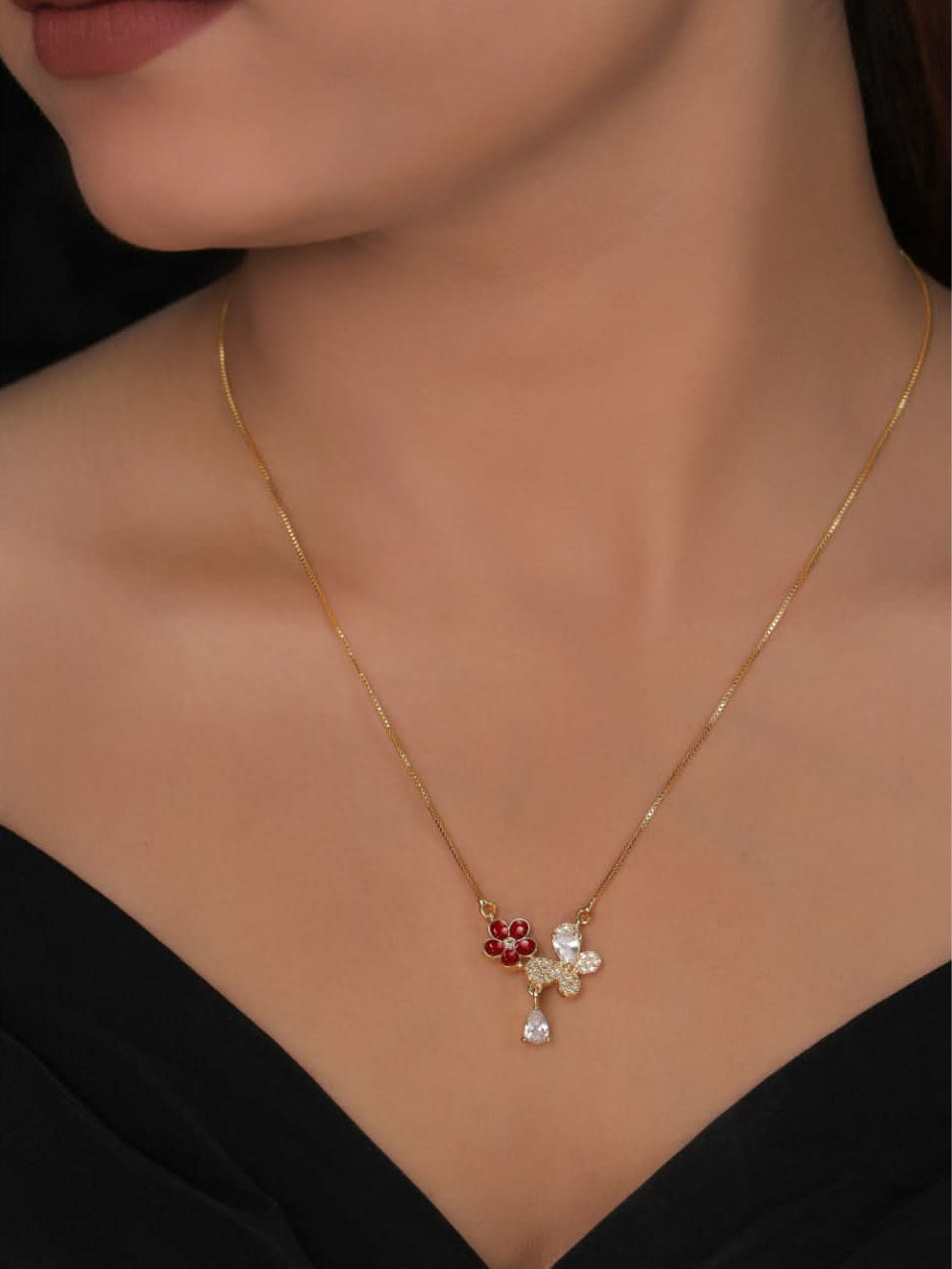 Gold necklace with a floral pendant featuring red and white stones on a model wearing a black top.