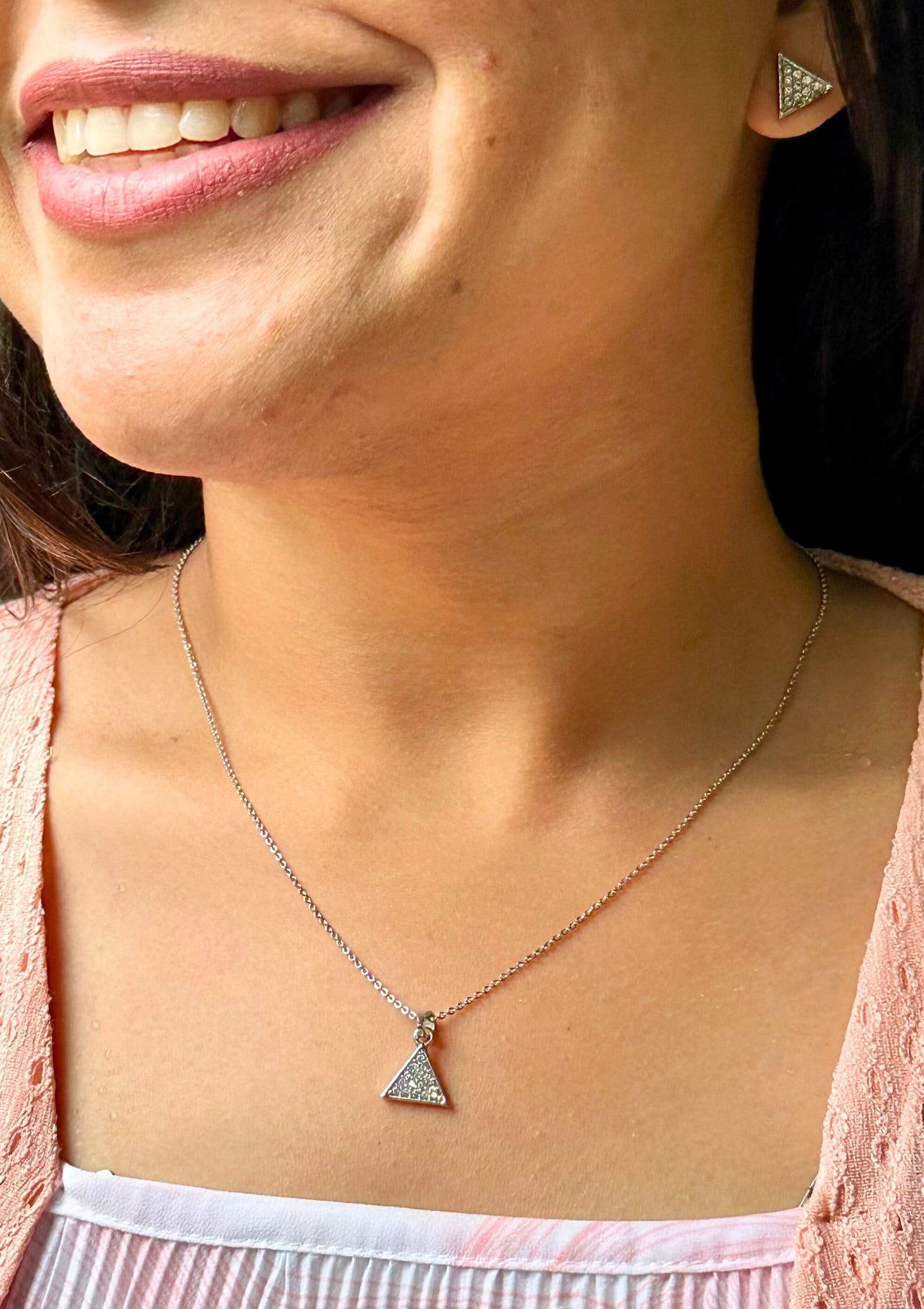 Close-up of a person wearing a necklace with a triangle silver pendant.