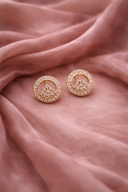 Rose gold earrings with gemstones on a soft pink fabric background