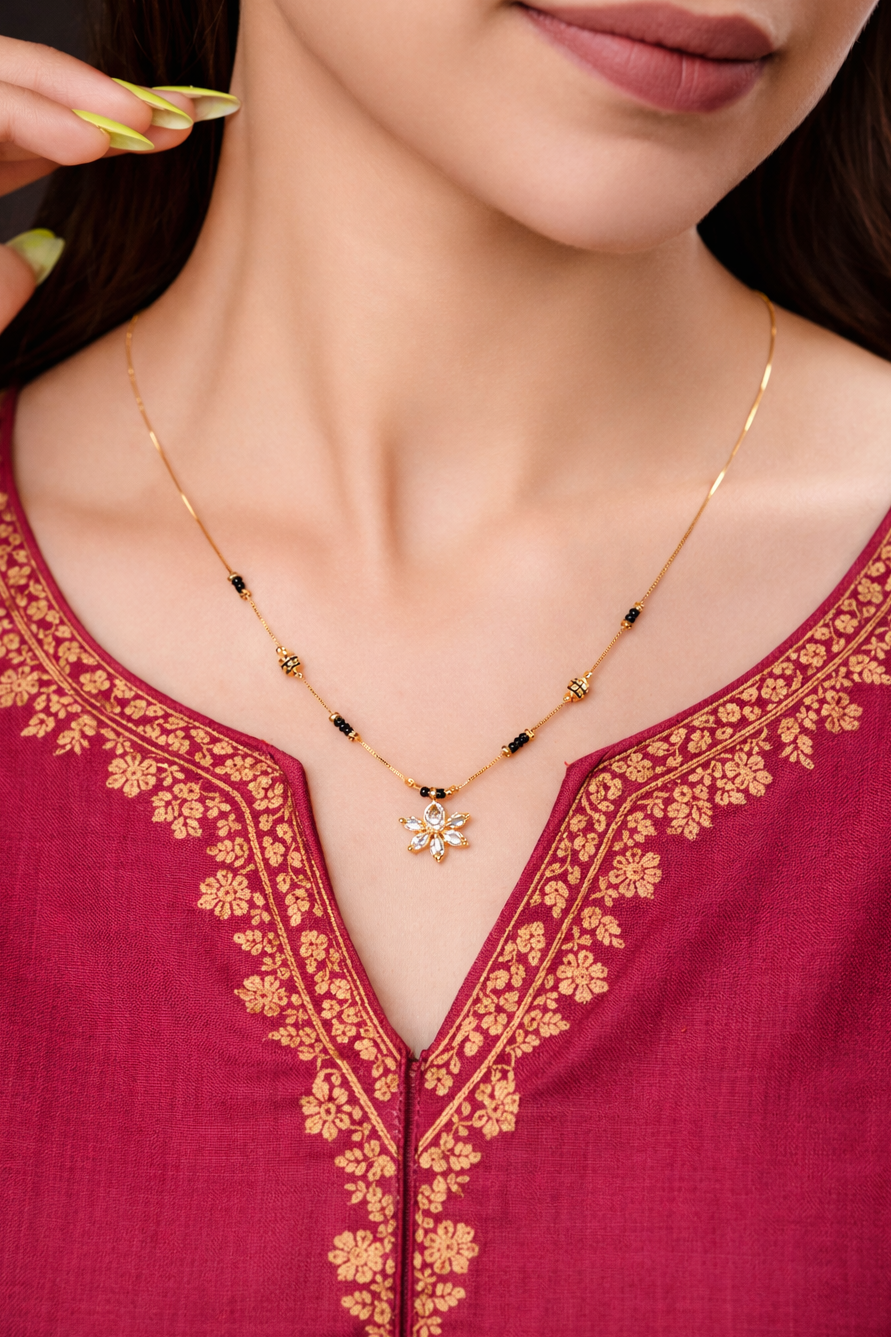 Close-up of a person wearing a gold necklace with a pink embroidered top.