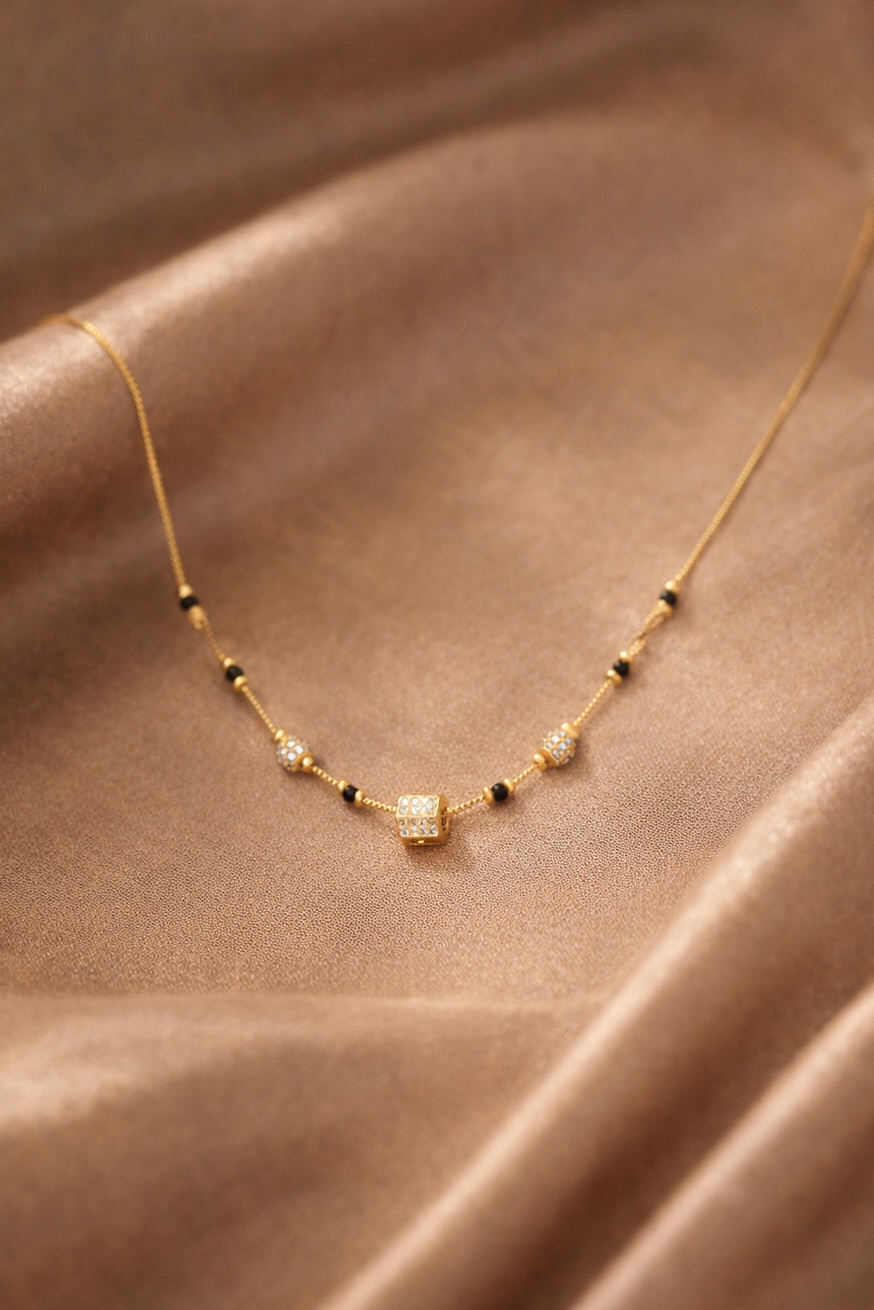 Gold necklace with black and clear beads on a brown fabric background