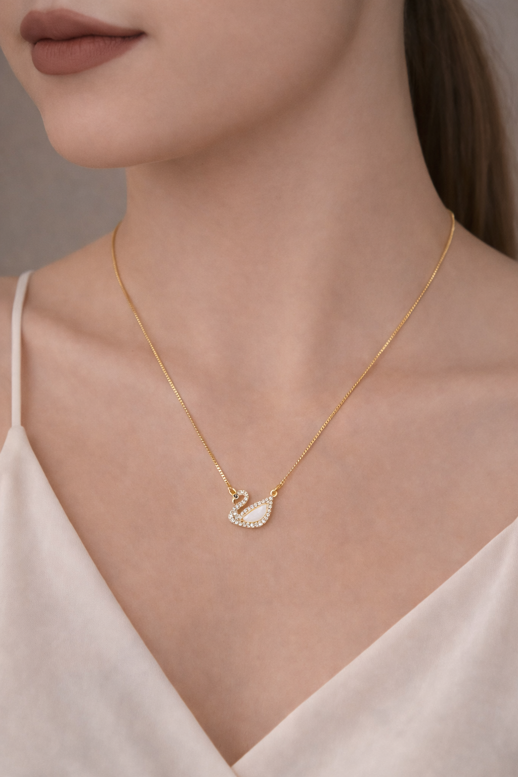 Gold necklace with a swan pendant worn by a model against a neutral background