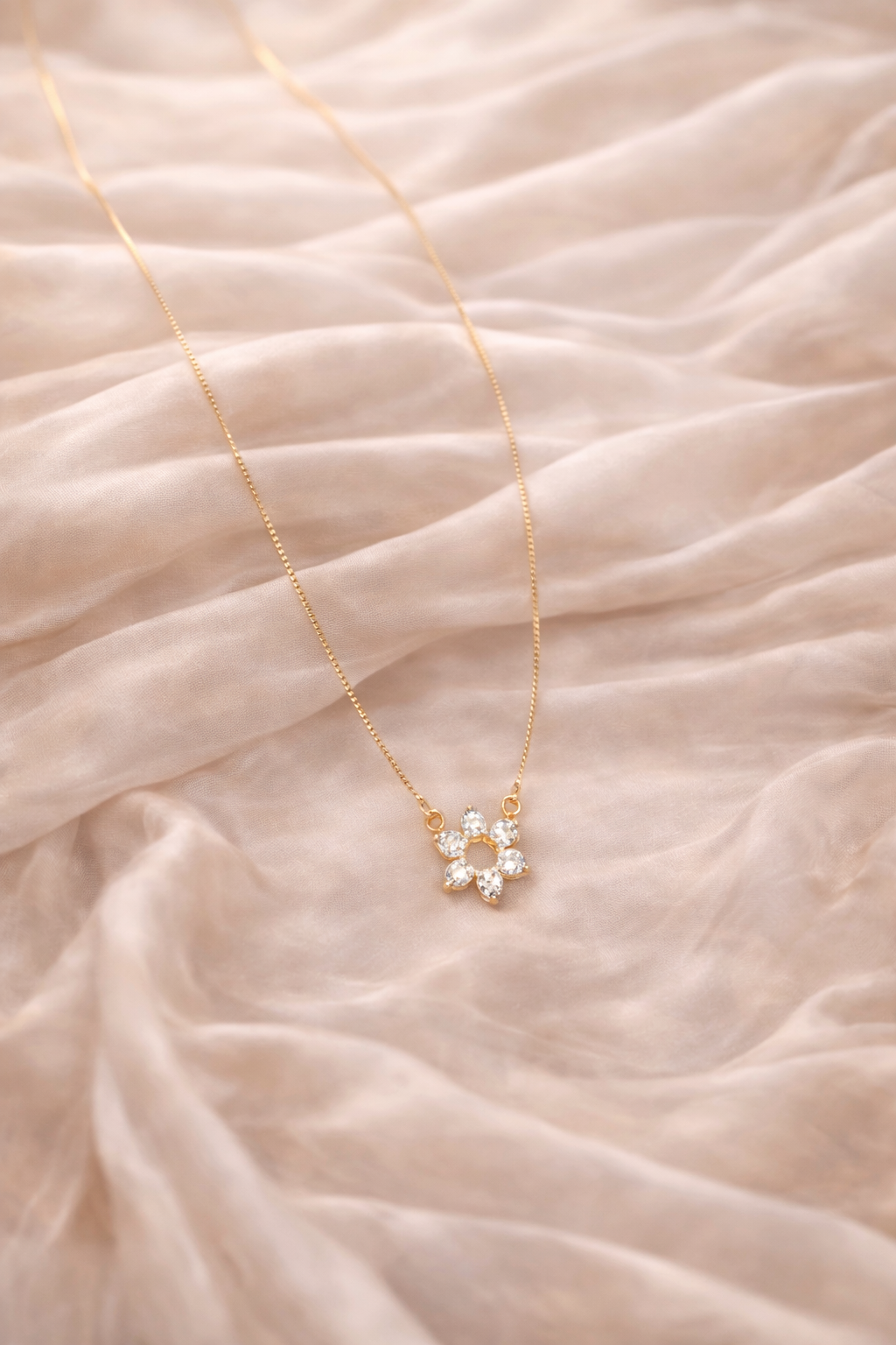 Gold necklace with a floral pendant on a soft pink fabric background