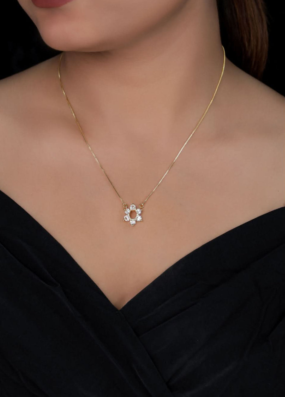 Gold necklace with a floral pendant worn by a person in a black dress.