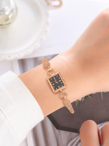 A close-up of a woman's wrist wearing a gold-tone watch with a square black dial and decorative crystal details on the bracelet.