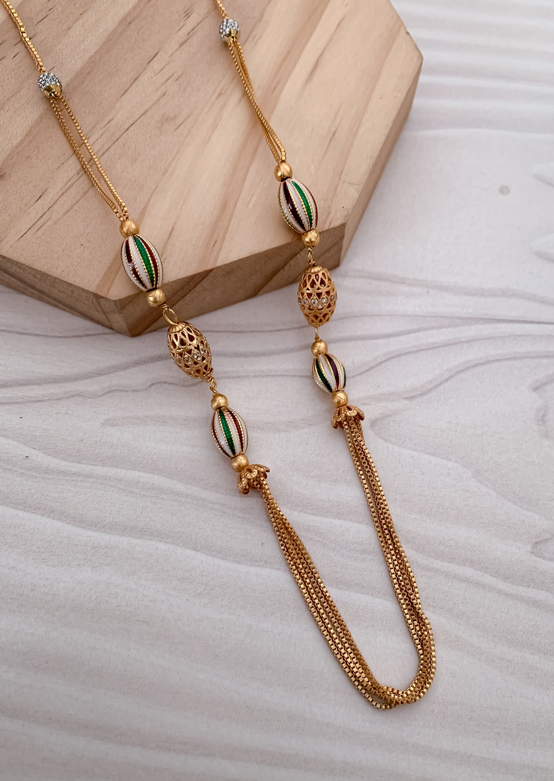 Gold necklace with decorative beads on a light wooden block