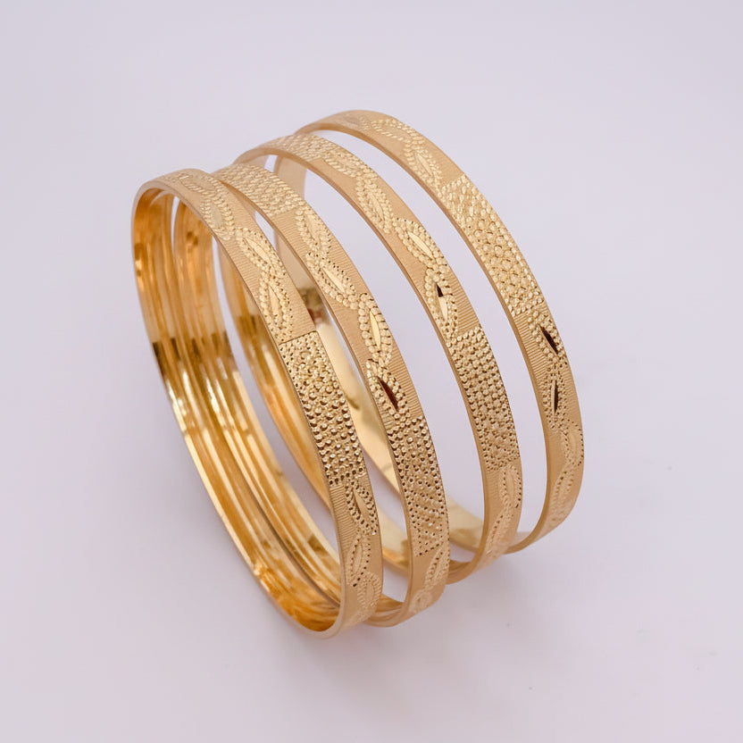 Gold bangles on a white surface with white flowers in the background