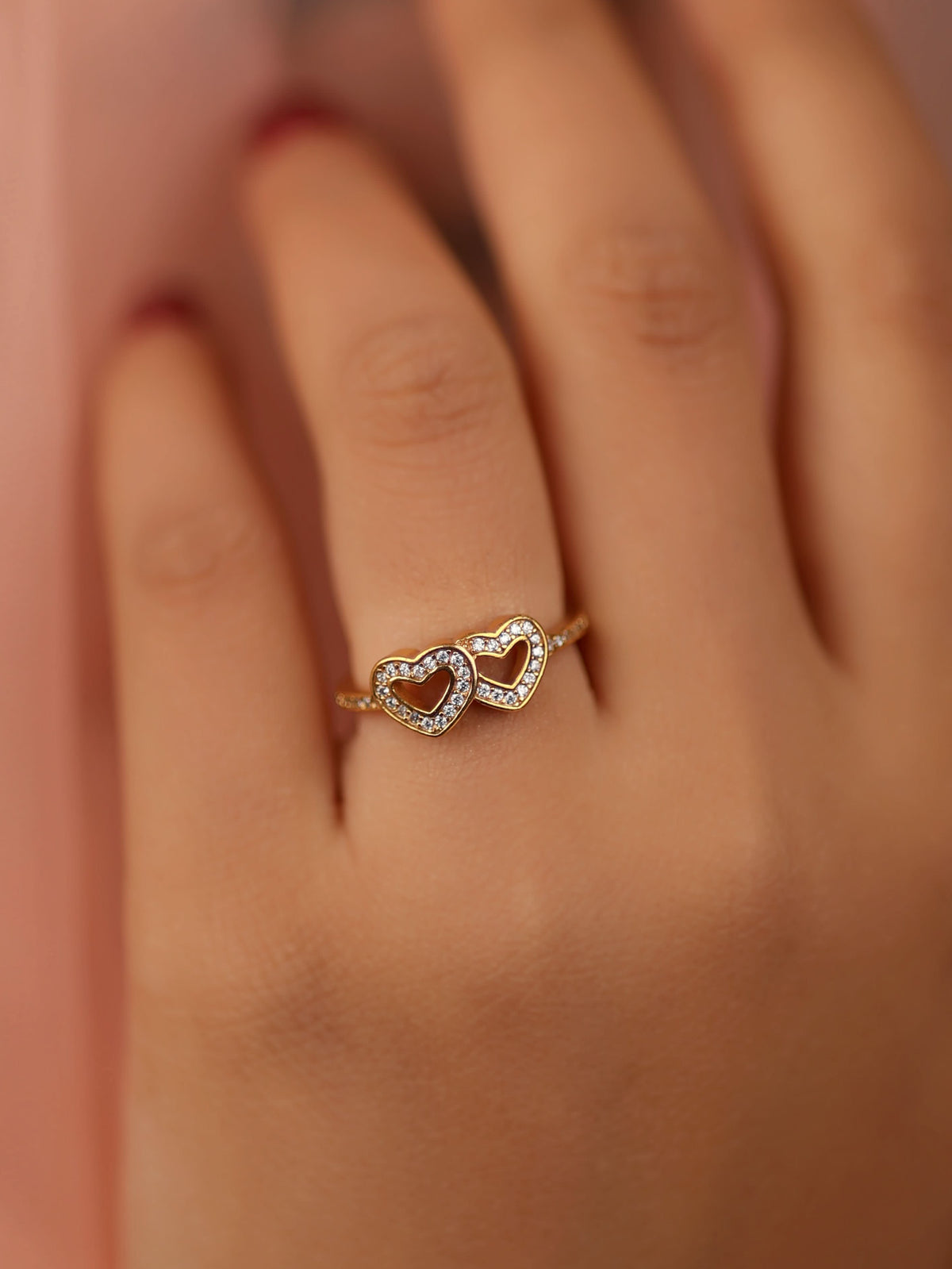 Hand wearing a gold ring with a heart design against a blurred background