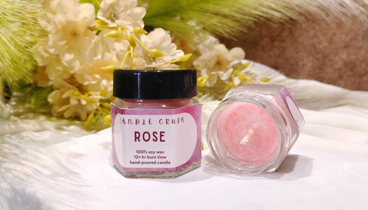 Two jars of 'Rose' scented candles on a soft fabric background with flowers.