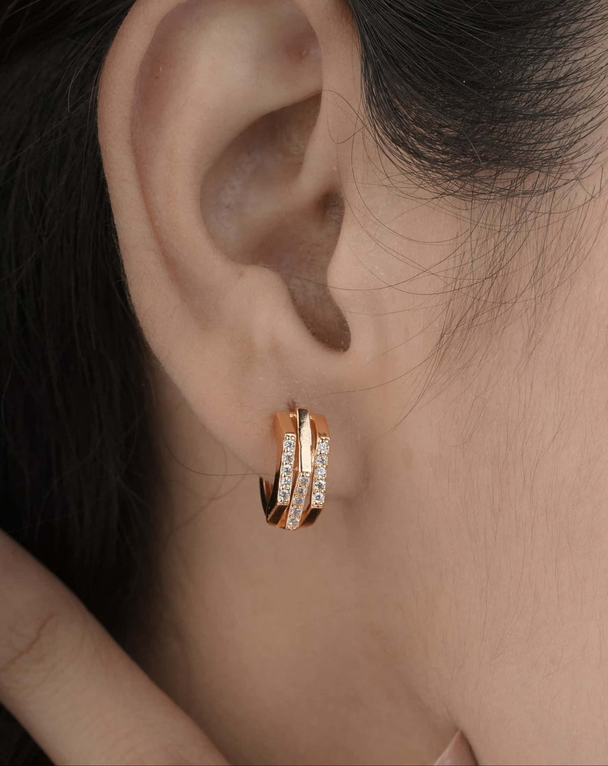 Close-up of a person wearing a gold hoop earring with a blurred background | Belleza Jewels