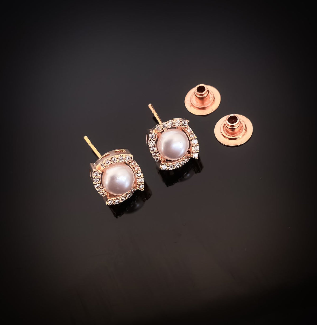 Pair of pearl earrings with rose gold settings on a black background