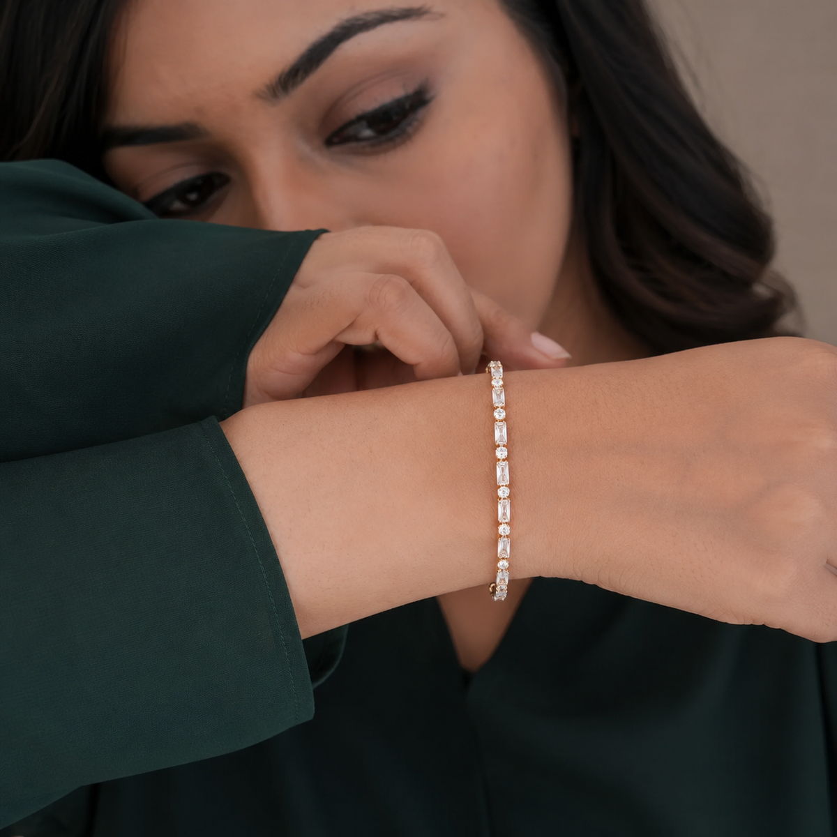 Woman in emerald wearing the gold baguette and round stone tennis bracelet