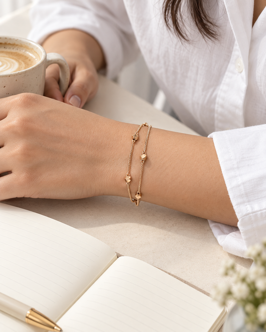 Geometric charm double-layer gold-tone bracelet worn on the wrist beside coffee and a notebook